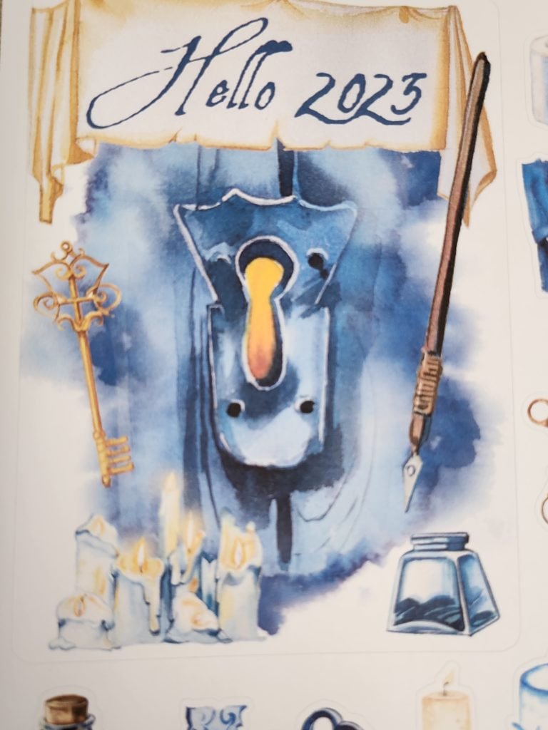 Image of a keyhole in a door with light shining through. Over it is a banner saying "Hello 2023". Added to the main image is a key, a dip pen and bottle of ink, and a bank of lit candles.